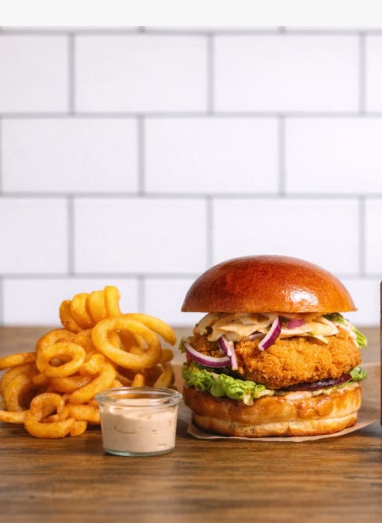 Burger med sprød kylling, coleslaw og rødløg ved siden af twister fries og en skål dip