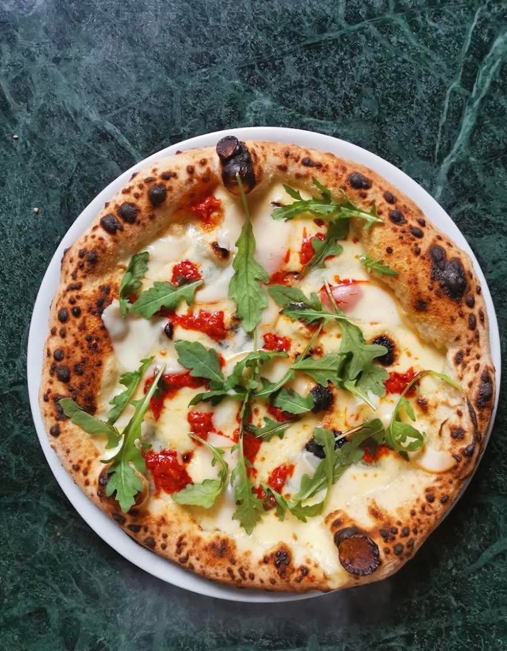 Hvid pizza med mozzarella, rucola og klatter af tomatsauce på en grøn marmorplade