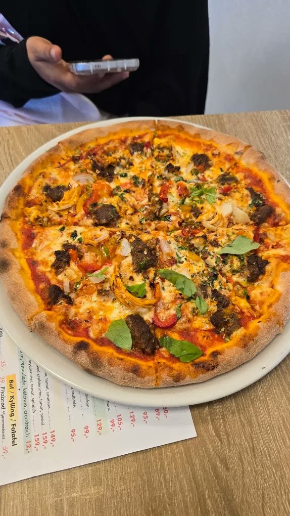 Pizza med kødstykker, peberfrugt, løg og frisk basilikum på en tallerken