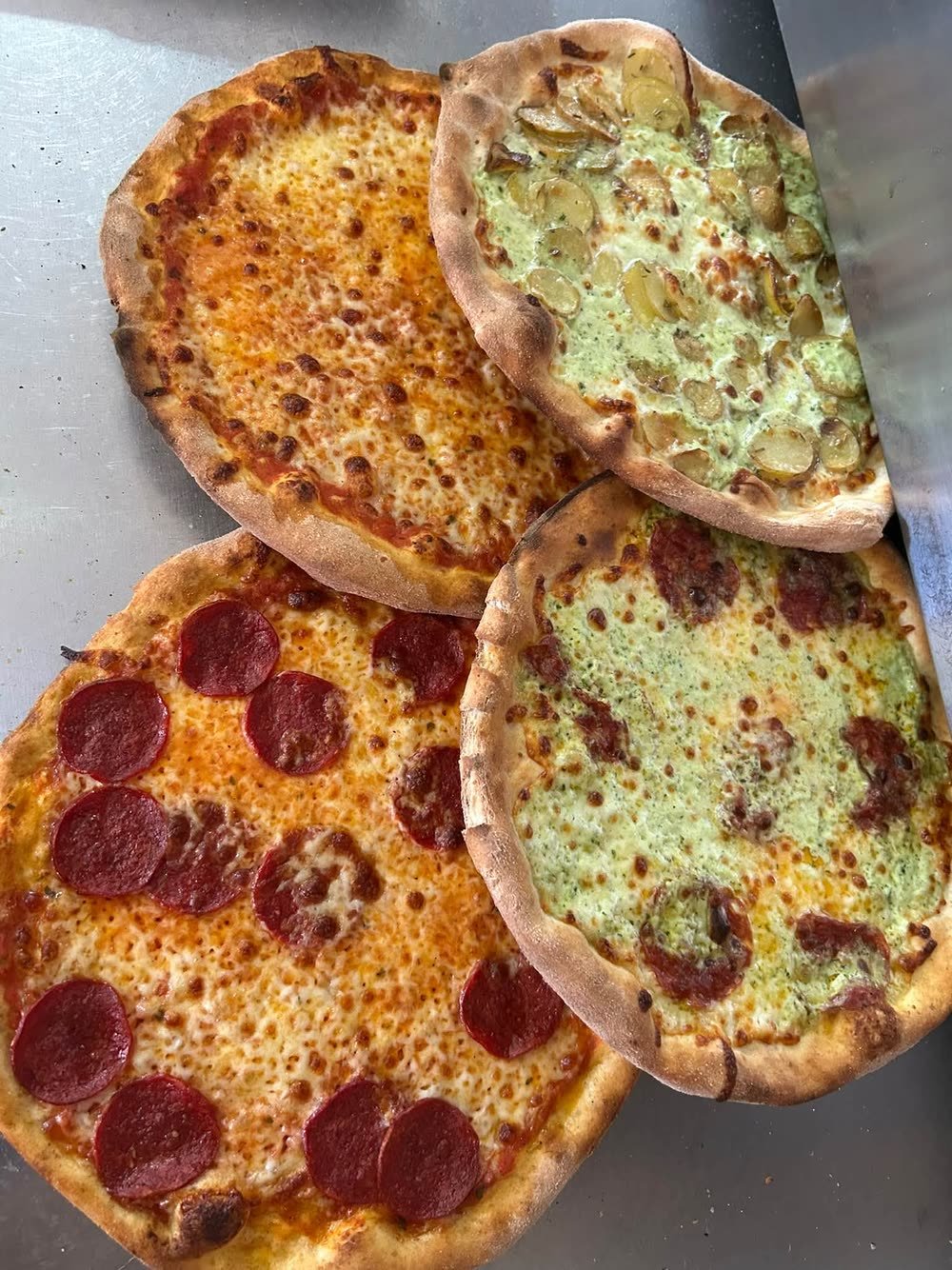 Fire nybagte pizzaer: margherita, pepperoni, en med kartofler og pesto, og en med pesto og pepperoni