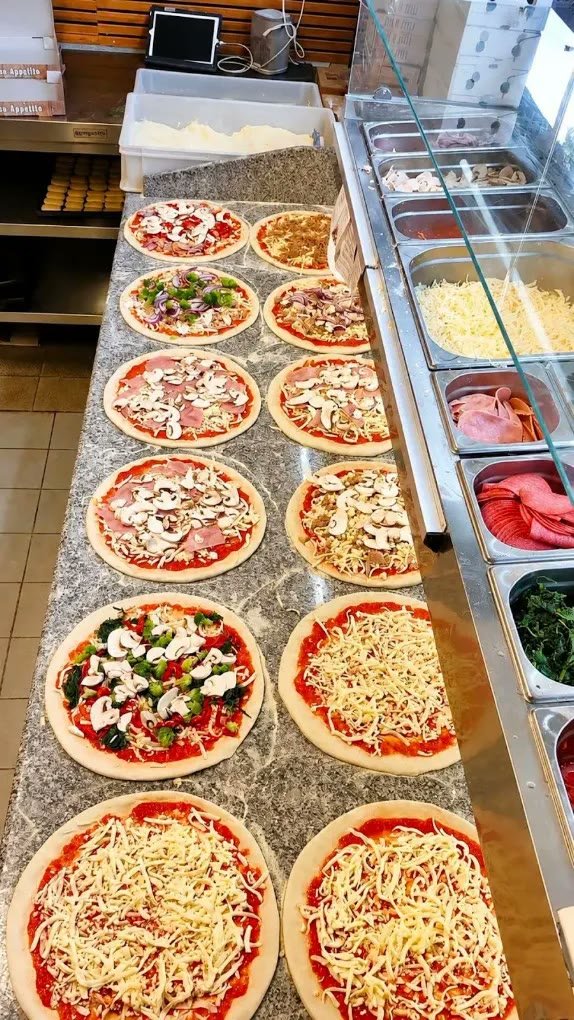 Rækker af friskbelagte pizzaer på marmorbordet ved siden af kølediskene med fyld