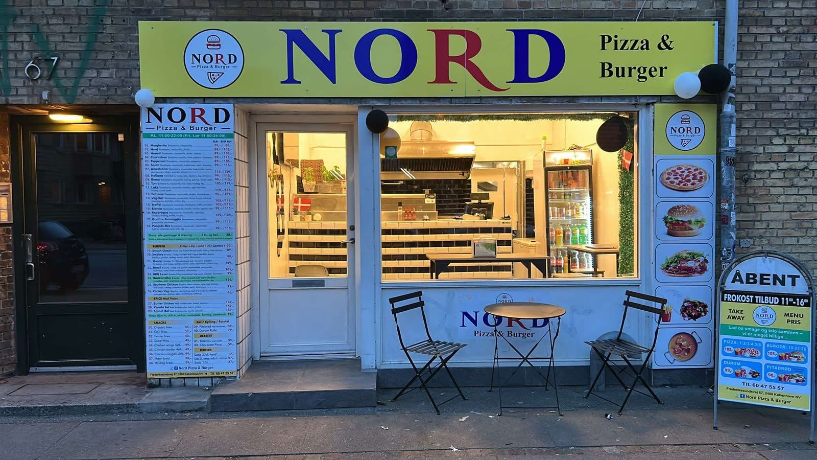 Facaden på NORD Pizza & Burger: gult skilt med blå bogstaver, menukortet i vinduet og et lille cafébord med to stole på fortovet
